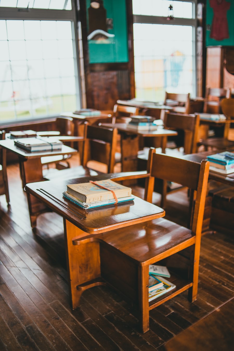 Sala de clases vacía con pupitres de madera y libros apilados